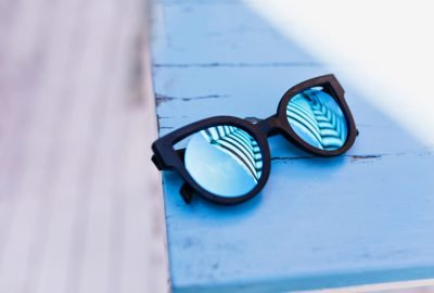Female sunglasses lying on blue wooden table. Blur portrait of trendy summer accessory.